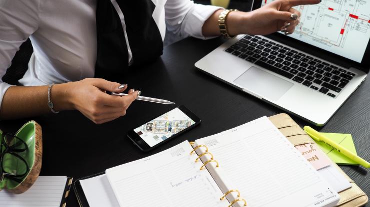 woman at a desk looking at architectural plans on a laptop